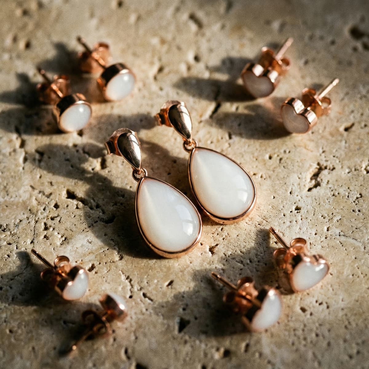 Rose gold and white resin teardrop drop earrings and heart stud keepsakes displayed on a textured stone surface, featuring a diy breastmilk earring making kit.