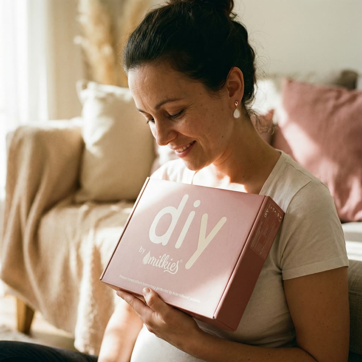 Mother at home holding a DIY by MILKIES box, highlighting why choosing a diy breastmilk earring making kit is a meaningful and convenient way to create a private keepsake.