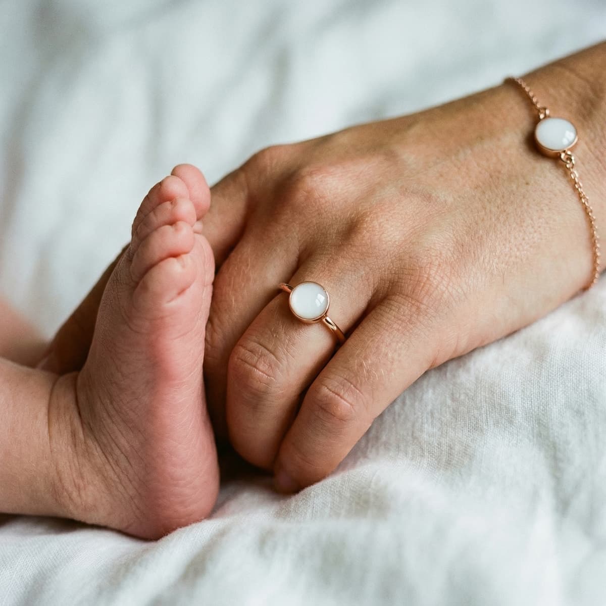 Close-up of a mother holding her baby’s feet while wearing a rose-gold ring and bracelet with milky white stones, inspiring moms who want to make your own breastmilk jewelry keepsake at home.