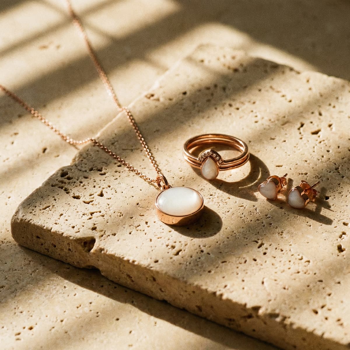 Rose gold necklace, ring, and heart stud earrings on a sunlit stone surface, showcasing how moms can make your own breastmilk jewelry as a lasting keepsake.