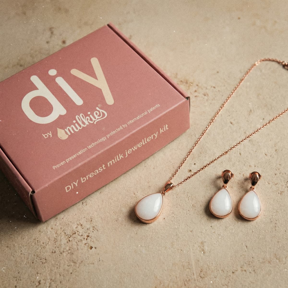 Flat lay of DIY by MILKIES breast milk jewellery kit box with rose-gold teardrop pendant necklace and matching earrings, perfect as new mom gifts for pregnant women to make a keepsake at home.